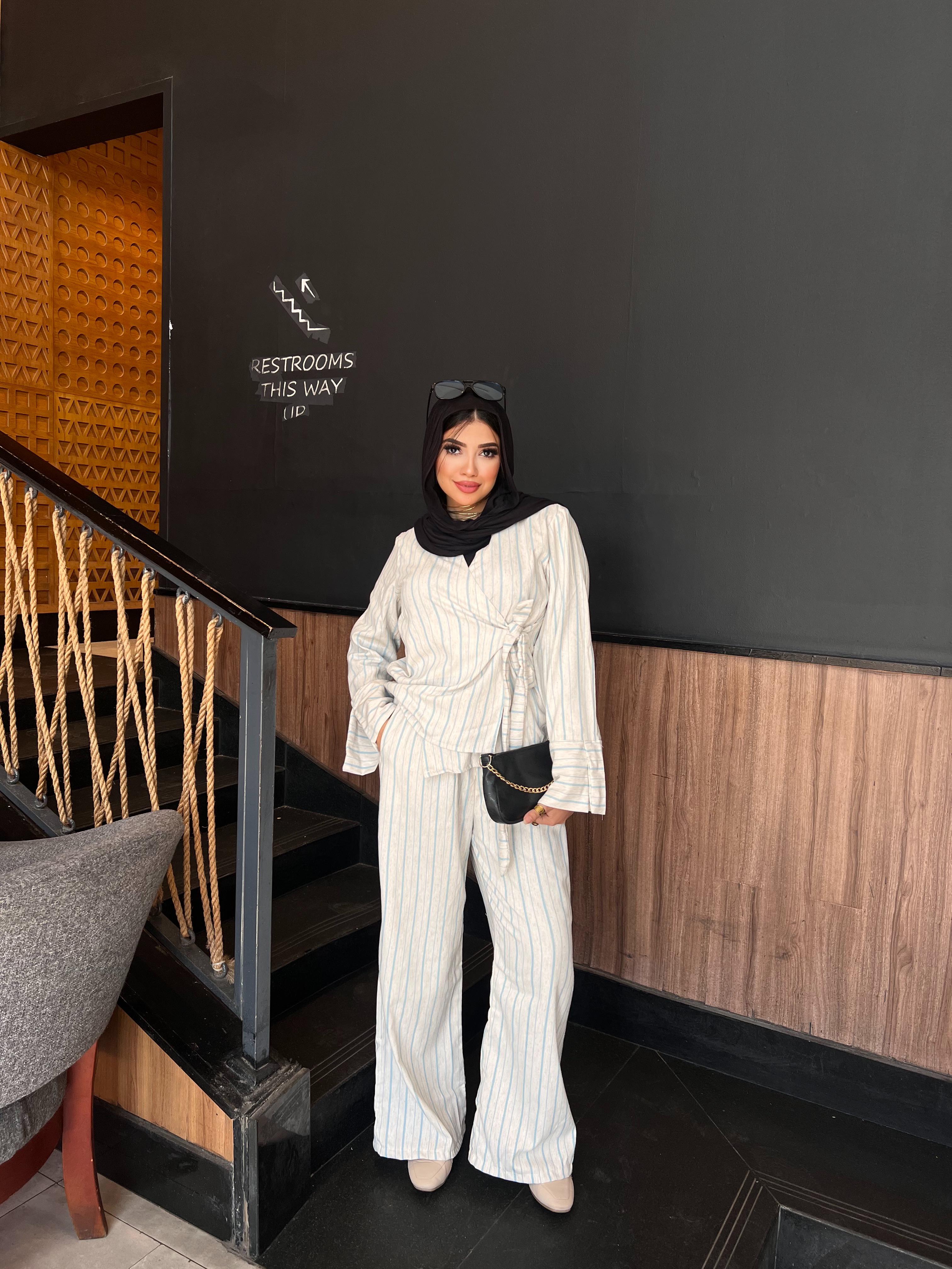 Woman in a white outfit standing in front of a black wall with 'Restrooms This Way' sign.