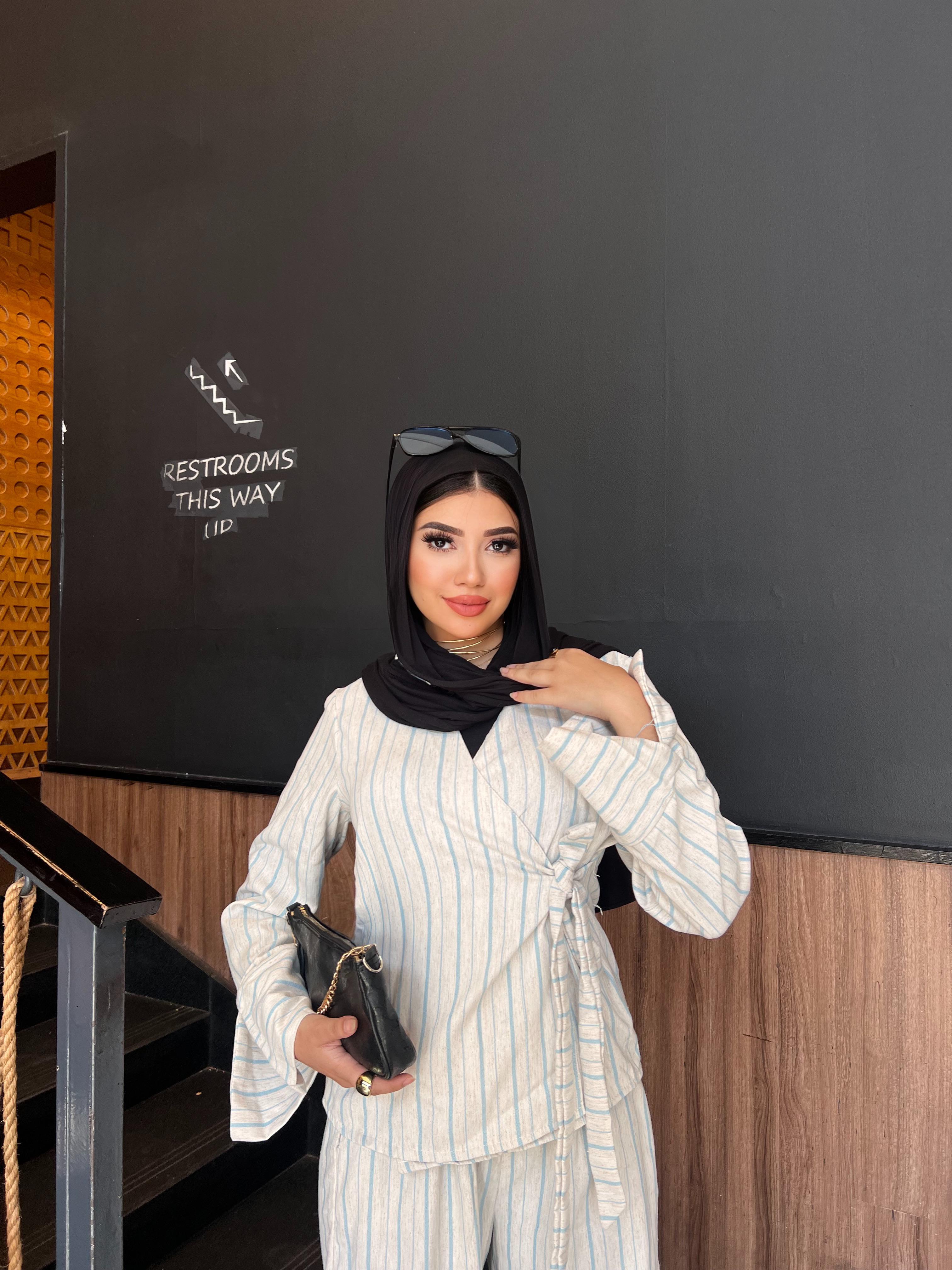 Woman in a striped outfit standing in front of a black wall with 'Restrooms This Way' sign.